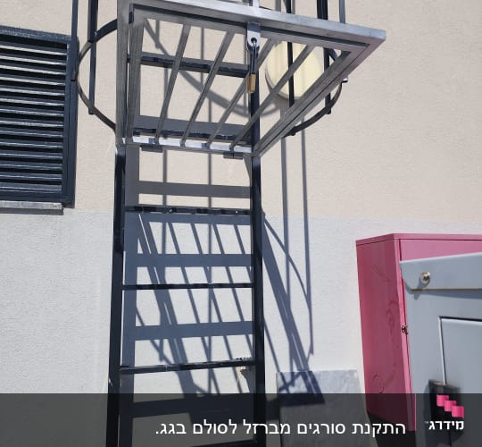 סולם טיפוס אנכי מברזל עם כלוב הגנה ושער נעול על קיר מבנה